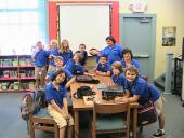 A group of students smiling around a large table inside.