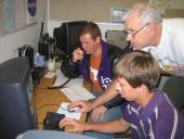 Two students sitting next to a radio with a teacher.